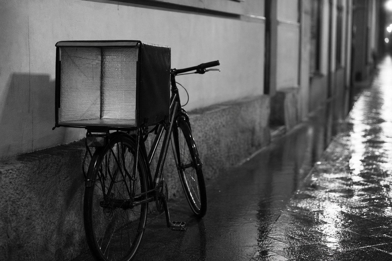 Geparkeerde fiets met een lege isolerende bezorgbox tegen een natte stadsmuur in de schemering