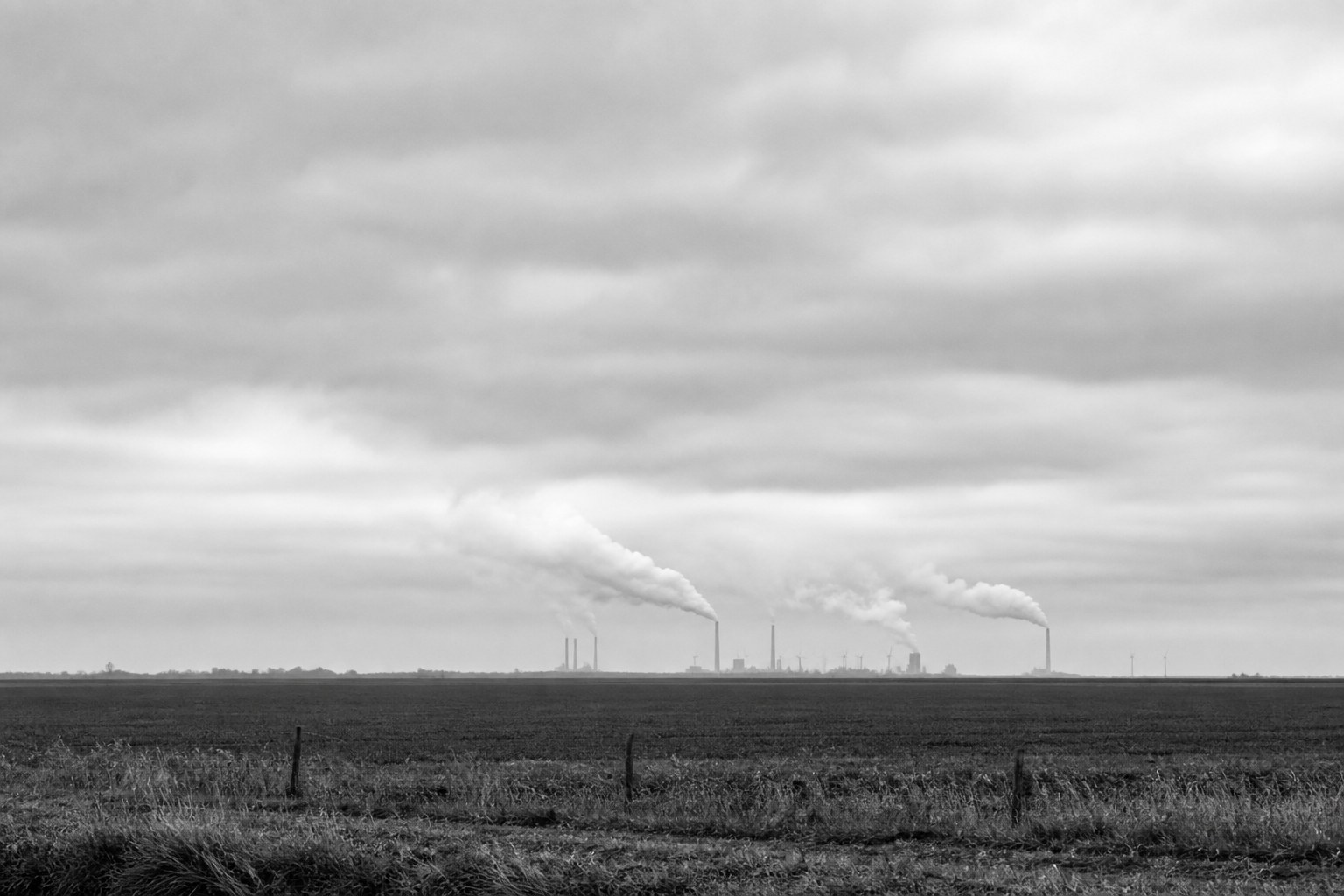 Industriele schoorstenen met rookpluimen aan de horizon van een leeg Nederlands polderlandschap
